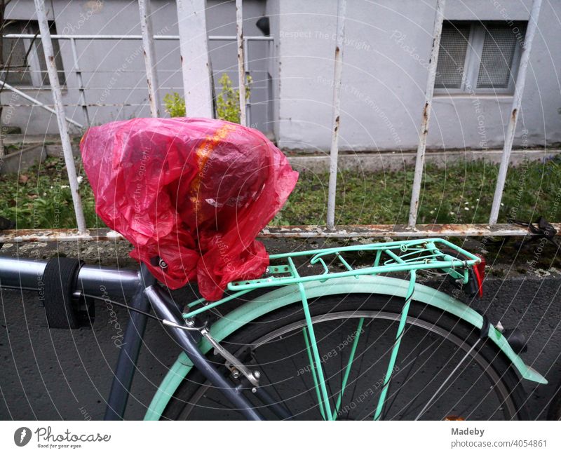 Bicycle in grey and turquoise with transparent red plastic bag over the saddle in front of an old iron fence in the north end of Frankfurt am Main in Hesse, Germany