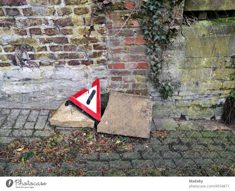 Broken warning triangle with big stones at the roadside on old cobblestones in front of brickwork in autumn in the old town of Oerlinghausen near Bielefeld in the Teutoburg Forest in East Westphalia-Lippe