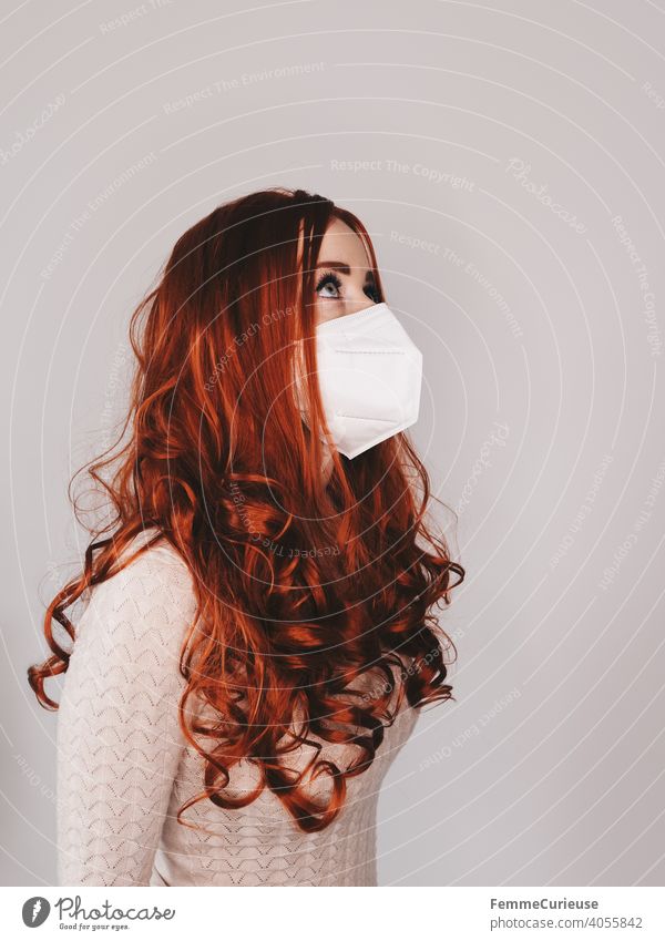 Woman with long red curly hair and FFP2 mask protective mask looks up in half profile Red-haired red hair ffp2 Mask Face mask guard sb./sth. covid-19 COVID