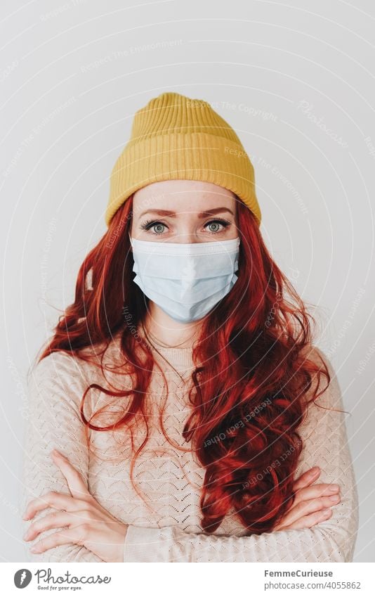 Woman with red long curly hair and yellow hipster beanie cap wears medical protection mask mouth guard and looks into camera medical mask Mask Mask obligation