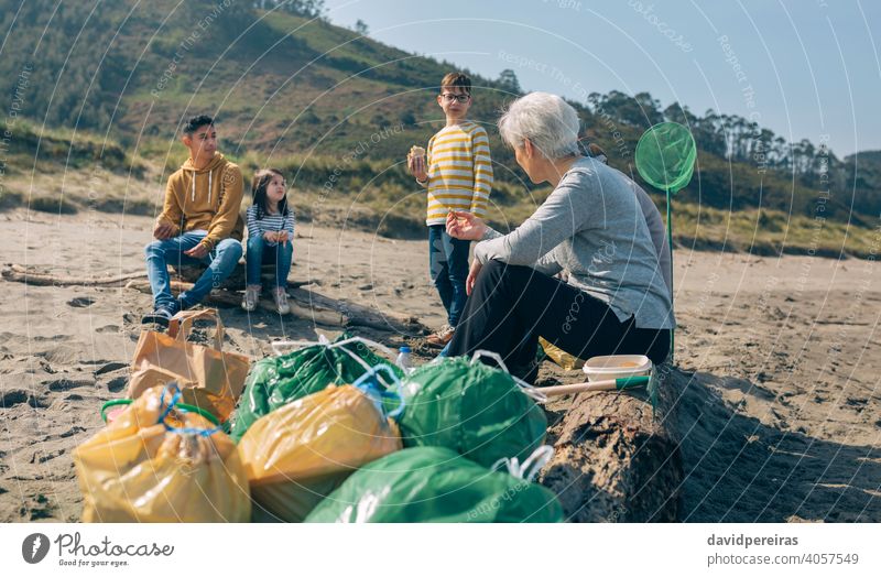 Volunteers resting after cleaning the beach trash bags volunteer group family eating pause break smiling coast talking enjoying garbage girl drinking litter