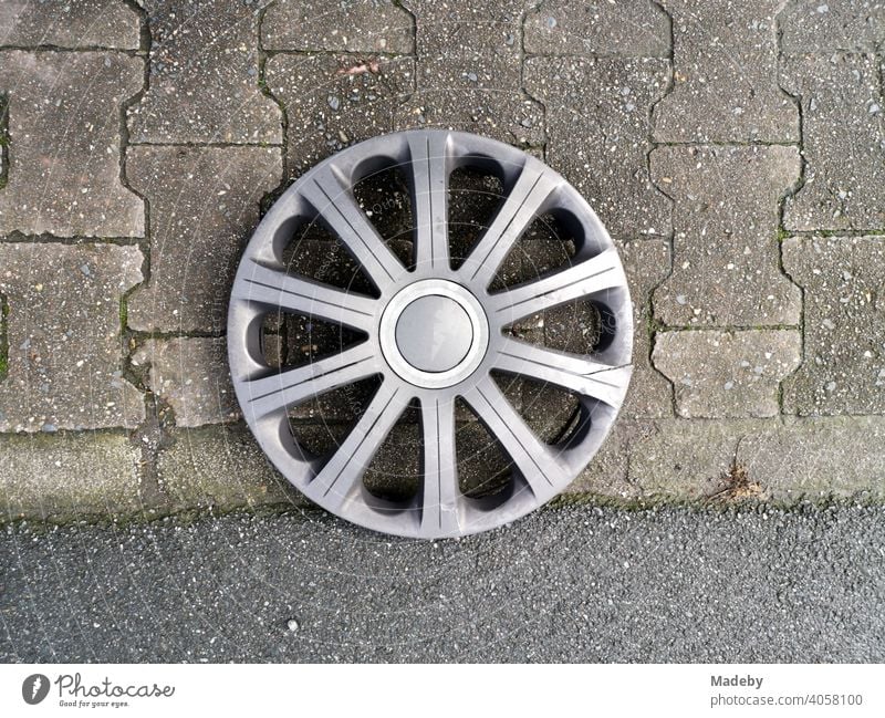Lost silver hubcap on the interlocking pavement at the Senckenberganlage in the Westend of Frankfurt am Main in Hesse Wheel Wheel cover Wheel rim Star Rim