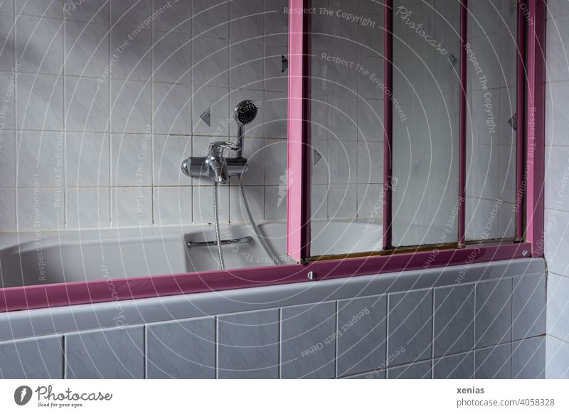 In the old bathroom is a senior inappropriate old bathtub with pink sliding doors, hand shower, handle and light tiles Bathtub Bathroom Hand shower bathe