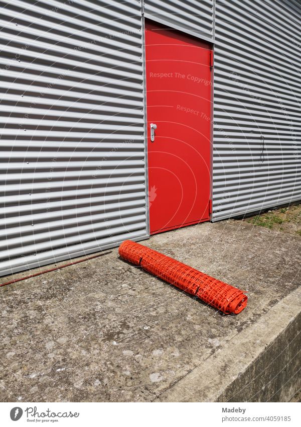 Red steel door in grey corrugated iron of a modern aircraft hangar with rolled-up barrier net in summer sunshine at the glider airfield Oerlinghausen near Bielefeld in the Teutoburg Forest in East Westphalia-Lippe