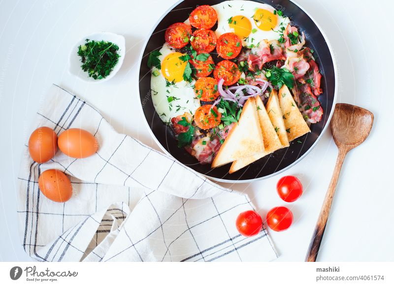 tasty comfort breakfast served in pan - fried eggs, cherry tomatoes, bacon, red onion and toasted bread. food meal meat cooked morning traditional dish