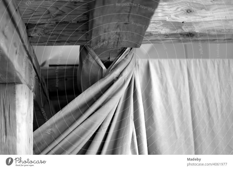 Beautiful old wooden roof beams under the roof and curtain with folds in a renovated farmhouse on a farm in Rudersau near Rottenbuch in the district of Weilheim-Schongau in Upper Bavaria, photographed in classic black and white
