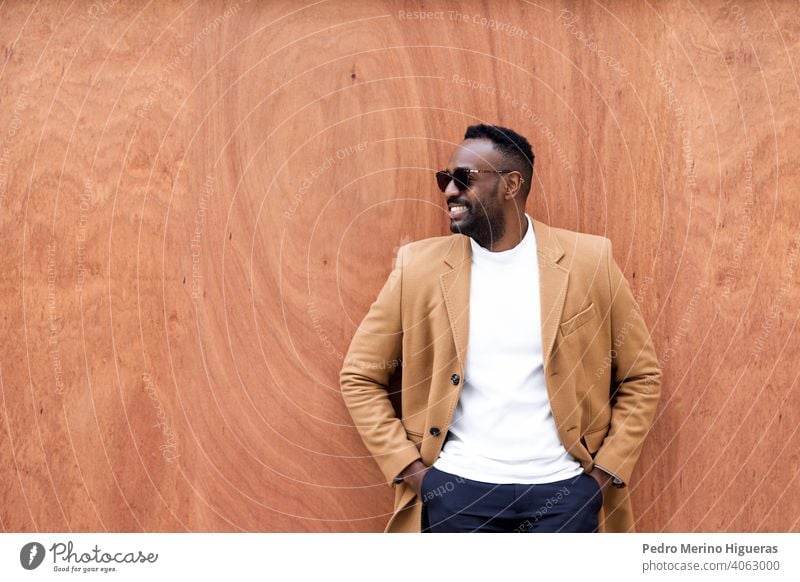 Handsome black man leaning against a wall looking aside smiling. african sunglasses leisure writing portrait city urban person lifestyle trendy standing male