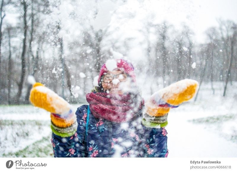 Woman throwing snow in the air and enjoying a cold winter day glasses outside natural healthy mitten scarf trees gloves one snowflake christmas beauty hat