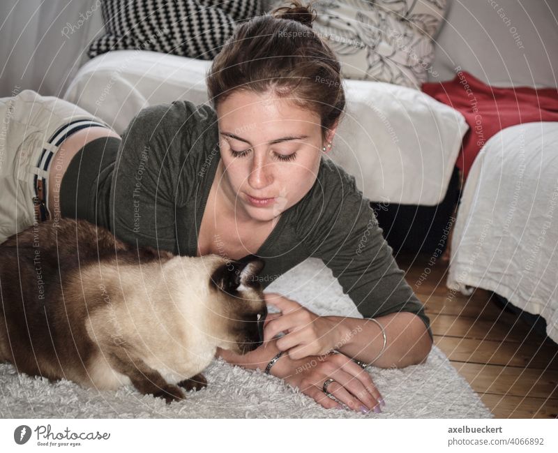 Young woman cuddles her Siamese cat lying on the floor Cat Pet Cozy at home Stroke Caress Cuddling Lifestyle relaxing Relaxation stay at home