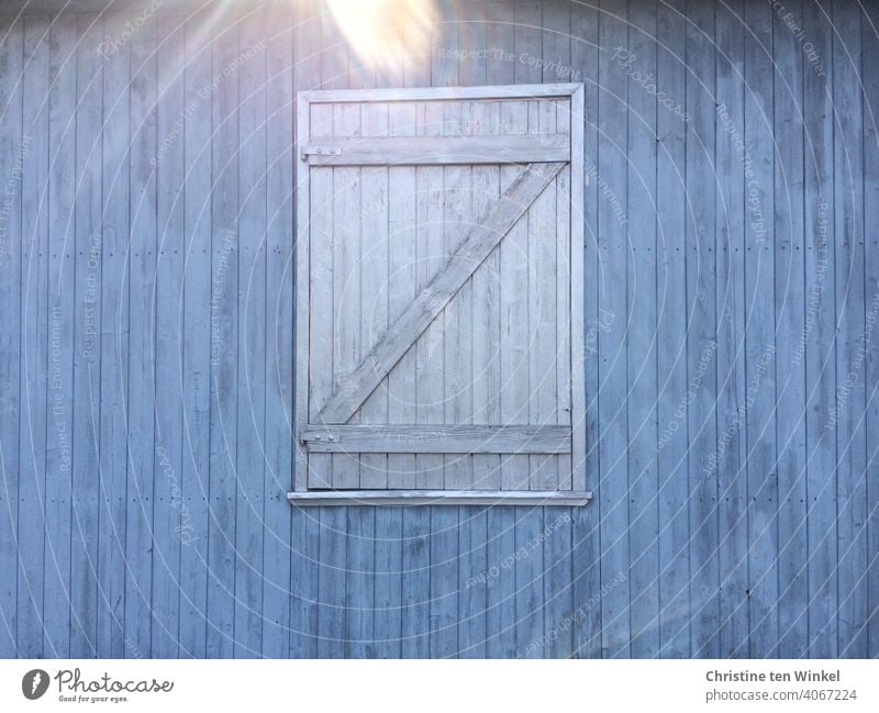 Blue wooden facade with grey closed wooden shutter. Reflection by incident sunlight at the upper edge of the picture Wooden facade Shutter Closed too Facade