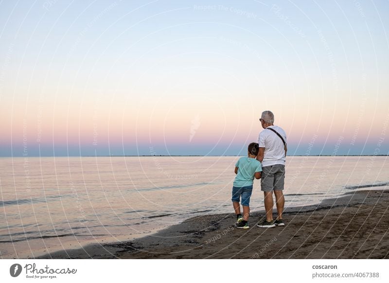 Grandfather and his grandson looking the ocean at sunset beach boy child childhood coast dad evening family freedom fun generation golden grandchild grandfather