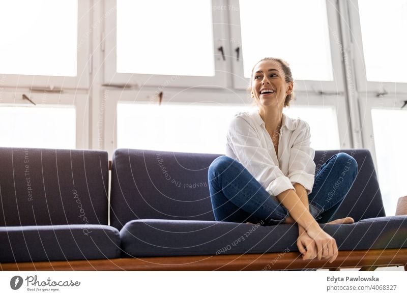 Young woman relaxing on sofa sitting couch resting comfortable break barefoot lotus yoga meditation millennials student hipster indoors loft window natural girl