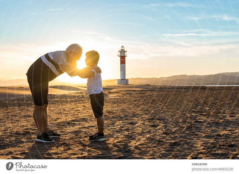 Grandfather and grandson hugging on a beach with a lighthouse in the background boy child childhood children coast dad day elderly family fangar far del fangar