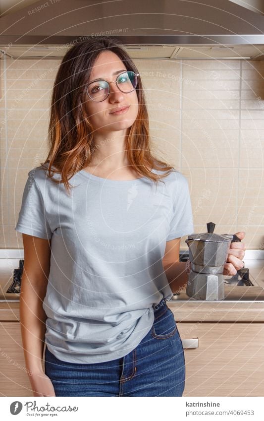 Young women stays in kitchen at home with coffee moka pot blue t-shirt wear mockup Lifestyle jeans glasses indoor round neck casual mock up italian alone Person