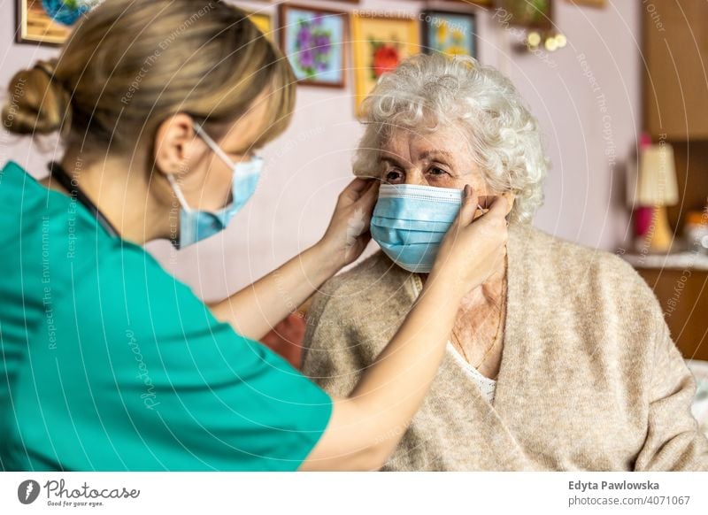 Female nurse helping a senior woman to put on protective face mask during home visit coronavirus real people covid elderly candid genuine mature female