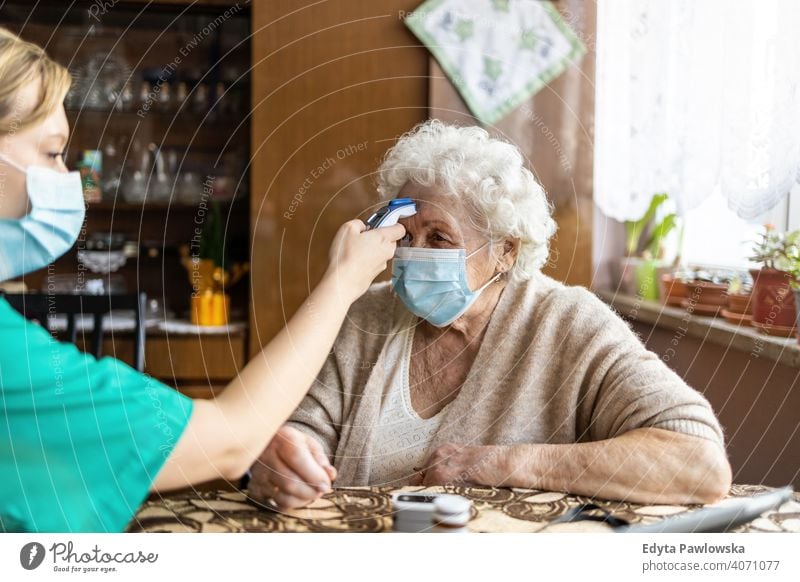Female nurse checking temperature to senior woman during home visit coronavirus face mask real people covid elderly candid genuine mature female Caucasian house