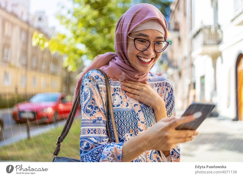 Smiling young muslim woman using mobile phone outdoors hijab headscarf islam arabic summer girl people young adult female lifestyle active millennial outside