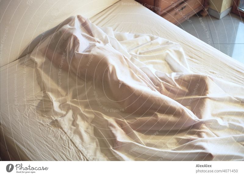 Young woman lying naked on a bed under a semi transparent blanket Woman Slim Athletic Articulated inside Room Bright daylight Esthetic Identity naturally Adults