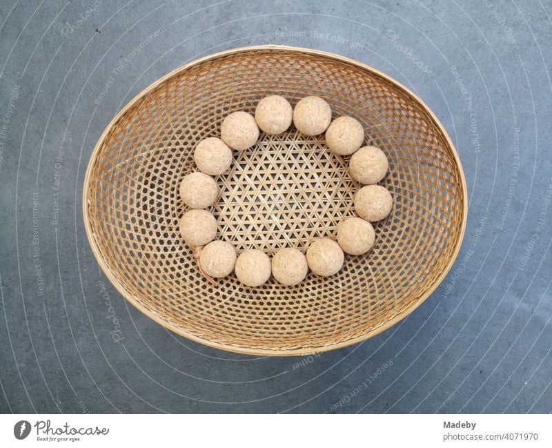Oval bast bowl in natural colours with a matching chain of wooden balls as a still life on a grey concrete floor in a designer apartment in Rudersau near Rottenbuch in the district of Weilheim-Schongau in Upper Bavaria