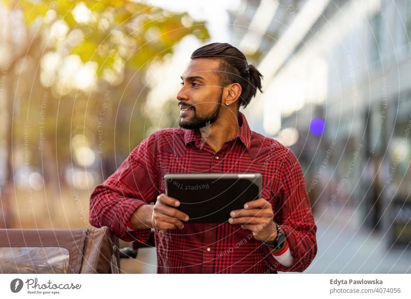 Young man using digital tablet outdoors at urban setting Sinhalese asian Indian bearded outside street standing city Warsaw one casual lifestyle guy attractive
