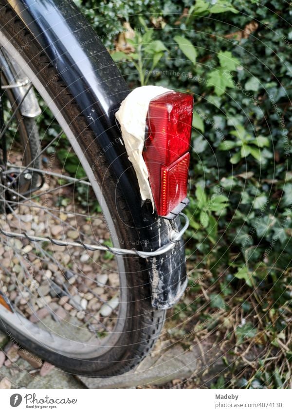 Red rear light fixed with adhesive tape to a black mudguard on a bicycle in front of a green hedge in Oerlinghausen near Bielefeld on the Hermannsweg in the Teutoburg Forest in East Westphalia-Lippe