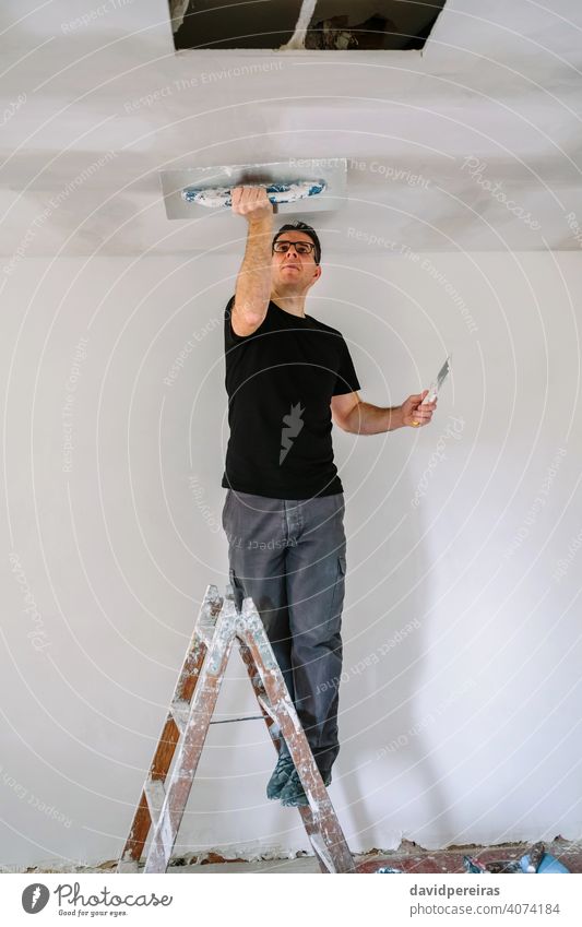 Plasterer smoothing plaster ceiling with the trowel mason professional plasterer climbed on ladder gypsum plaster spatula working builder construction