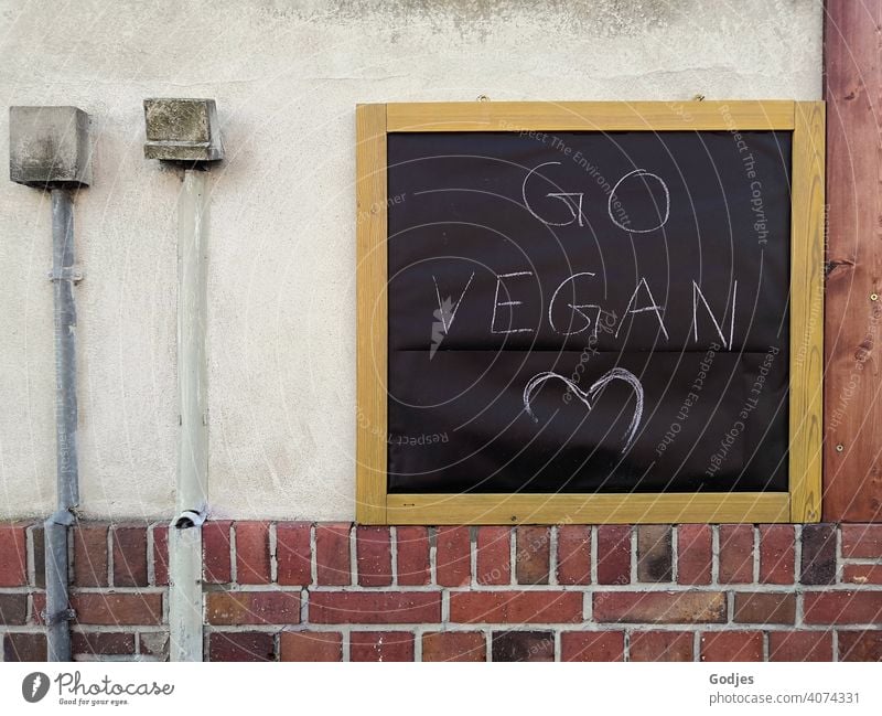 Board on a house wall with the inscription 'go vegan' next to it are cable ducts with distribution boxes Blackboard cable shaft wiring harness Sockets Heart