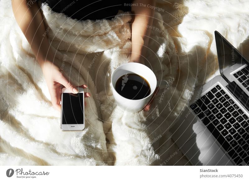 Young woman drinking coffee at home in her bed and checking her smartphone laptop cup computer typing young education lying girl hand girls person sitting