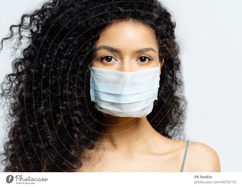Serious Afro American woman tries to stop virus and epidemic disease, stays at home during infectious outbreak, wears medical mask, isolated on white background, being hospitalized, diagnosed