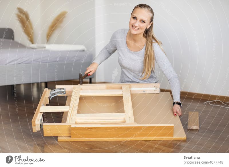 Happy woman collects furniture with a hammer in the bedroom assembling home young girl adult assembly diy moving indoors new craft tool wood female people