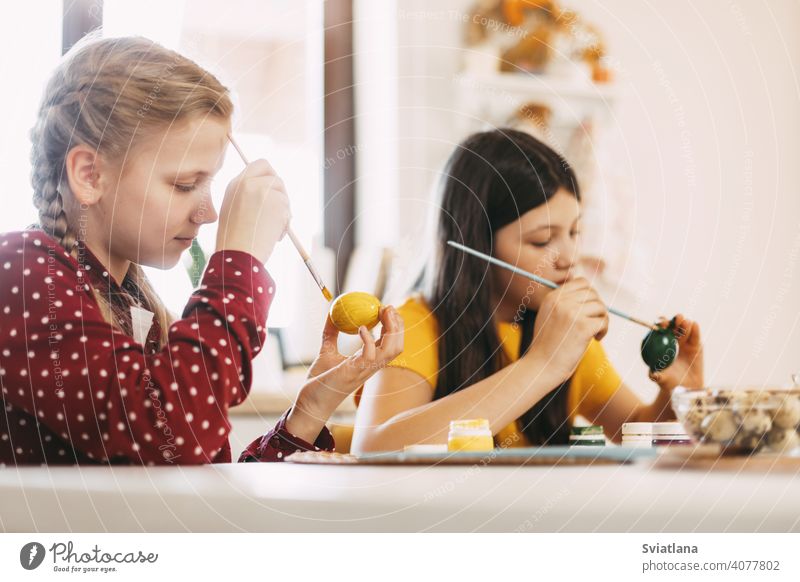 Two sisters are sitting at the table and painting Easter eggs in different colors for Easter, close-up easter spring child holiday preparation bright family