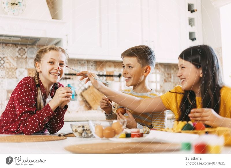 Two sisters and a brother are sitting at the table and painting Easter eggs in different colors for Easter, laughing and indulging easter spring child holiday