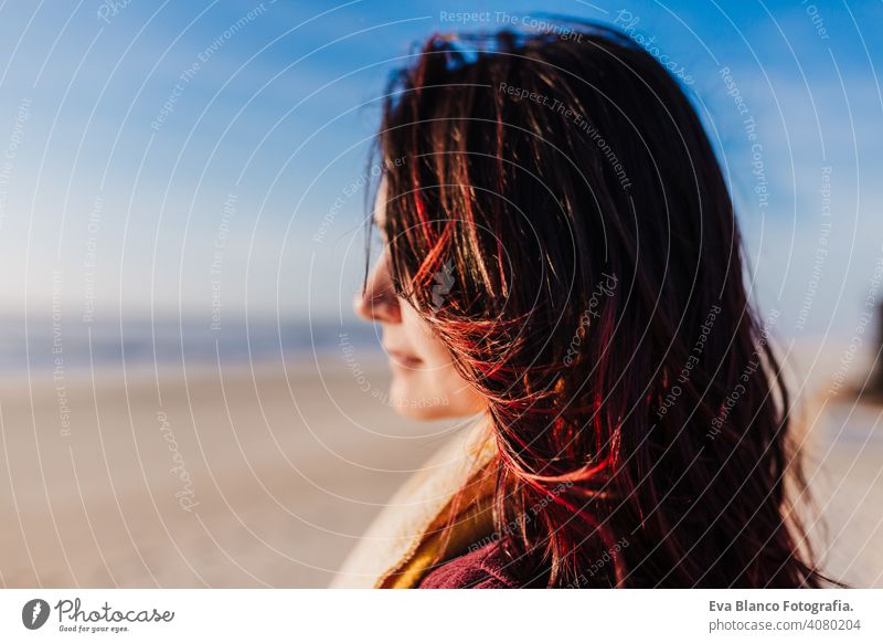 young caucasian woman relaxing at the beach at sunset. Selective focus on hair flying on a windy day. Holidays and relaxation concept portrait selective focus