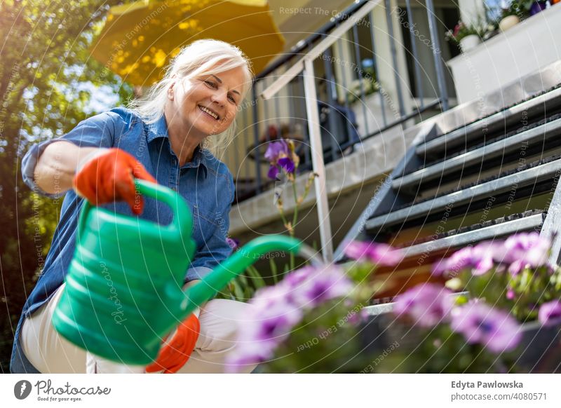 Senior woman watering plants in her garden smiling happy enjoying positivity vitality confidence people senior mature casual female Caucasian elderly home house