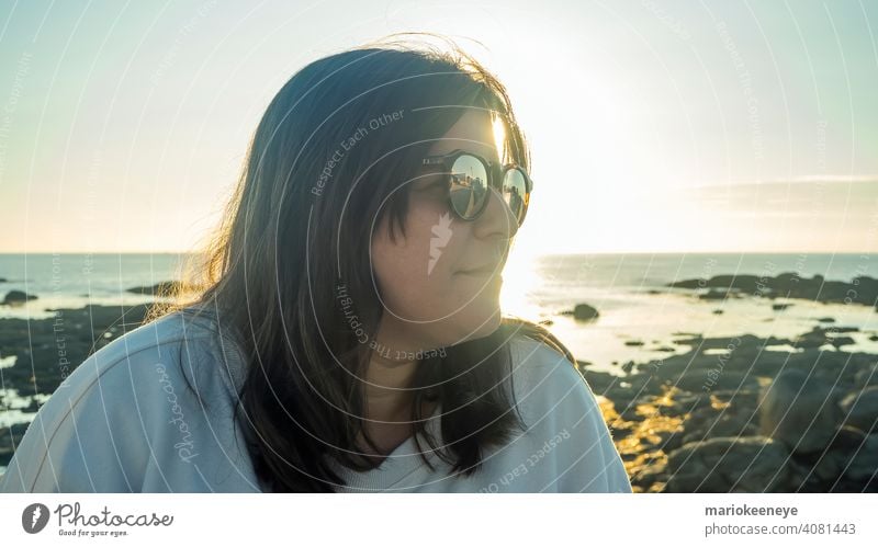 Side close-up of a Caucasian woman wearing sunglasses during a sunset by the sea close up caucasian one woman only lifestyle color image copy space sunshine