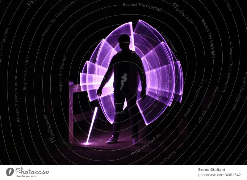 Silhouette of a man standing with a lightsaber with neon drawings and leds at lightpainting boy abstract illustration silhouette energy sphere concept purple