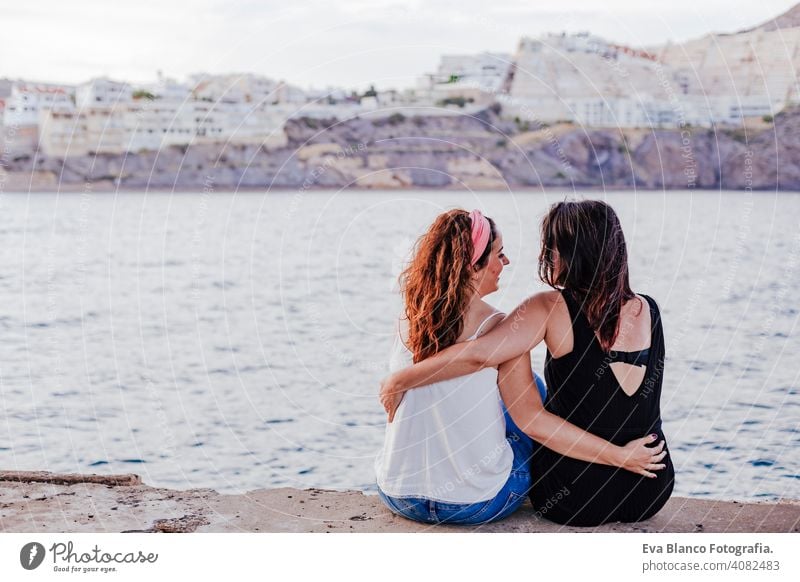 two women friends sitting by the beach hugging. lifestyle concept outdoors casual gay urban cheerful girlfriend standing couple young affection woman people