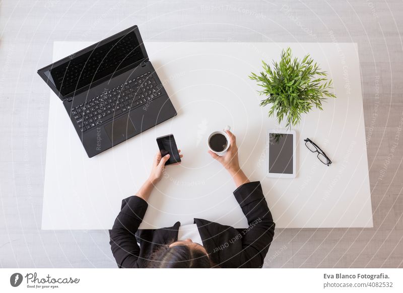 top view of a young business woman working at the office with mobile phone and holding a cup of coffee. Daytime. Lifestyles. Indoors computer laptop worker