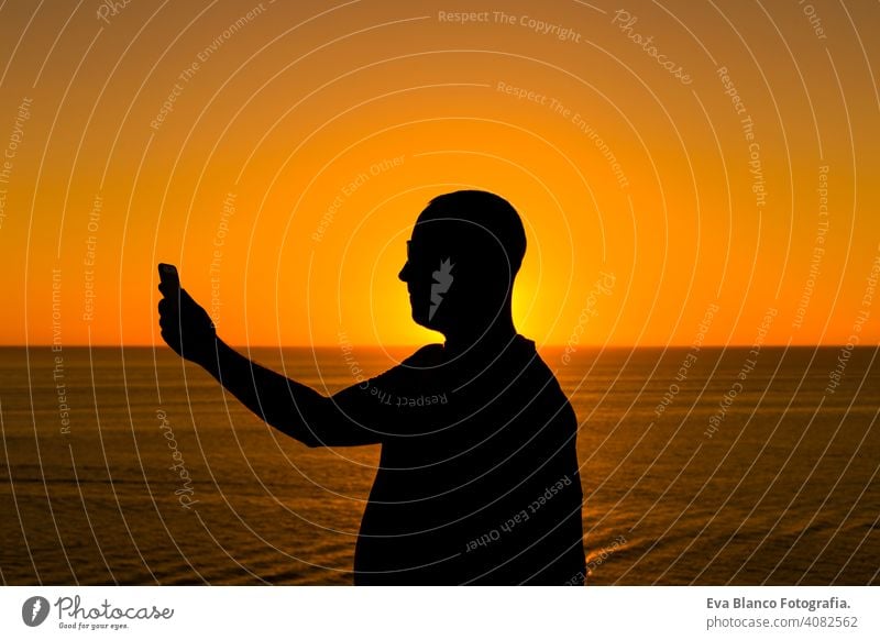 silhouette of a young man using mobile phone at sunset. Ocean background. Vacation and technology concept hand cell telephone person tourist people mountain