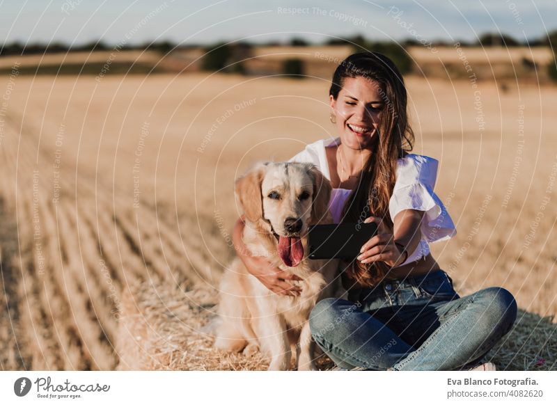 young beautiful woman walking with her golden retriever dog on a yellow field at sunset. Nature and lifestyle outdoors summer fashion beauty happy people nature