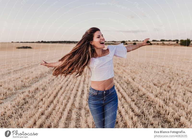 Summer Girl enjoying nature on yellow field. Beautiful young woman dancing Outdoors. Long hair in the wind. Happiness and lifestyle. Back view sunset beauty