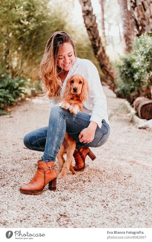 young woman and her cute puppy of cocker spaniel outdoors in a park dog pet sunny love hug smile kiss breed purebred beautiful blonde brown lifestyle portrait
