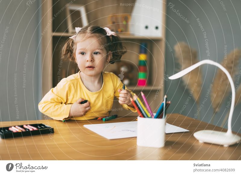 A little girl draws at the table with colored pencils at home or in kindergarten. Childhood, creativity, education. paper cute desk child kid childhood