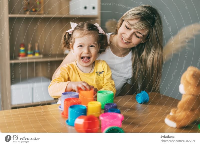 Mom and a laughing little girl play with colorful molds at the table at home. Time together, motherhood, parenthood child game build pyramid preschool mom