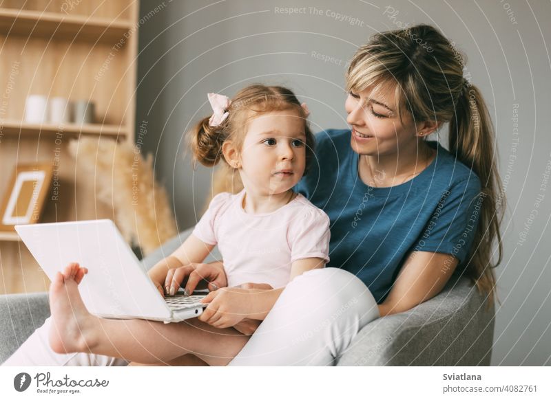A little girl and her mom watch cartoons on a laptop while sitting in a chair together child computer online internet kid baby freelancer notebook