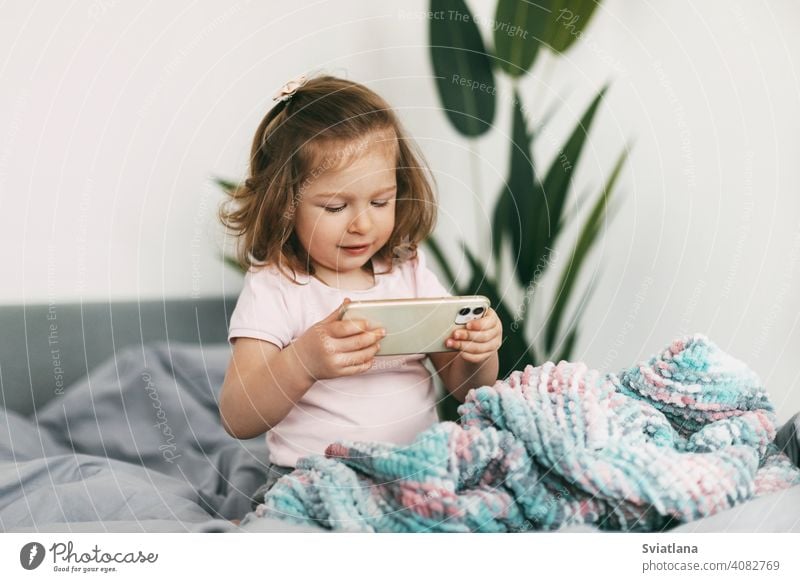 A little girl watches cartoons on her phone or plays on the bed before going to bed smartphone child kid mobile home small communication looking bedtime people