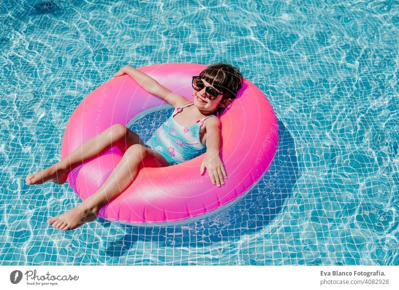 beautiful kid girl floating on pink donuts in a pool. Wearing sunglasses and smiling. Fun and summer lifestyle activity beauty outdoor teenager swimming