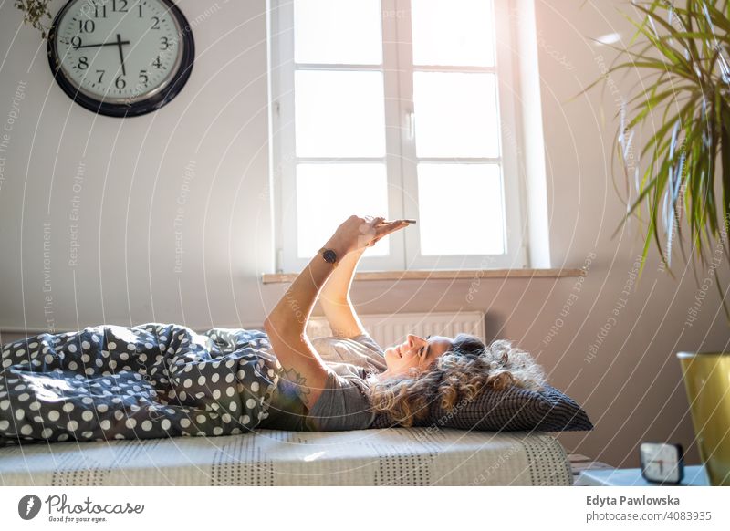 Young woman using smartphone in bed morning clock resting relaxation sleeping awake alarm clock sleepy waking up apartment leisure bedroom house home alone