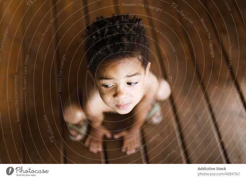 Black boy sitting on wooden floor home looking away black shirtless cozy child kid lumber timber cute sweet adorable innocence african american ethnic lifestyle