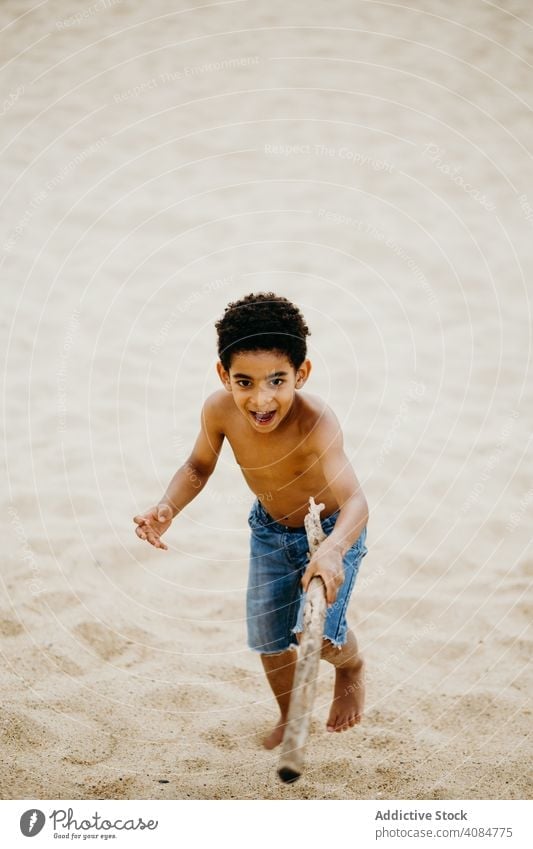 Black boy playing on beach sea sticks fun summer water shirtless barefoot kid child siblings game happy weekend lifestyle leisure shore coast ocean wet joy